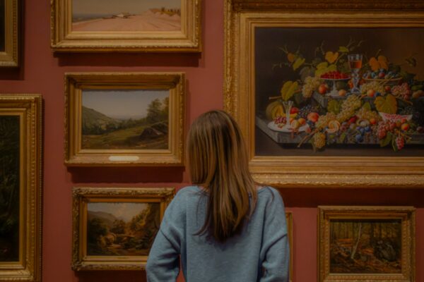 Kvinde betragter indrammede malerier på en museumsvæg i varmt lys