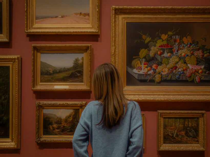 Kvinde betragter indrammede malerier på en museumsvæg i varmt lys